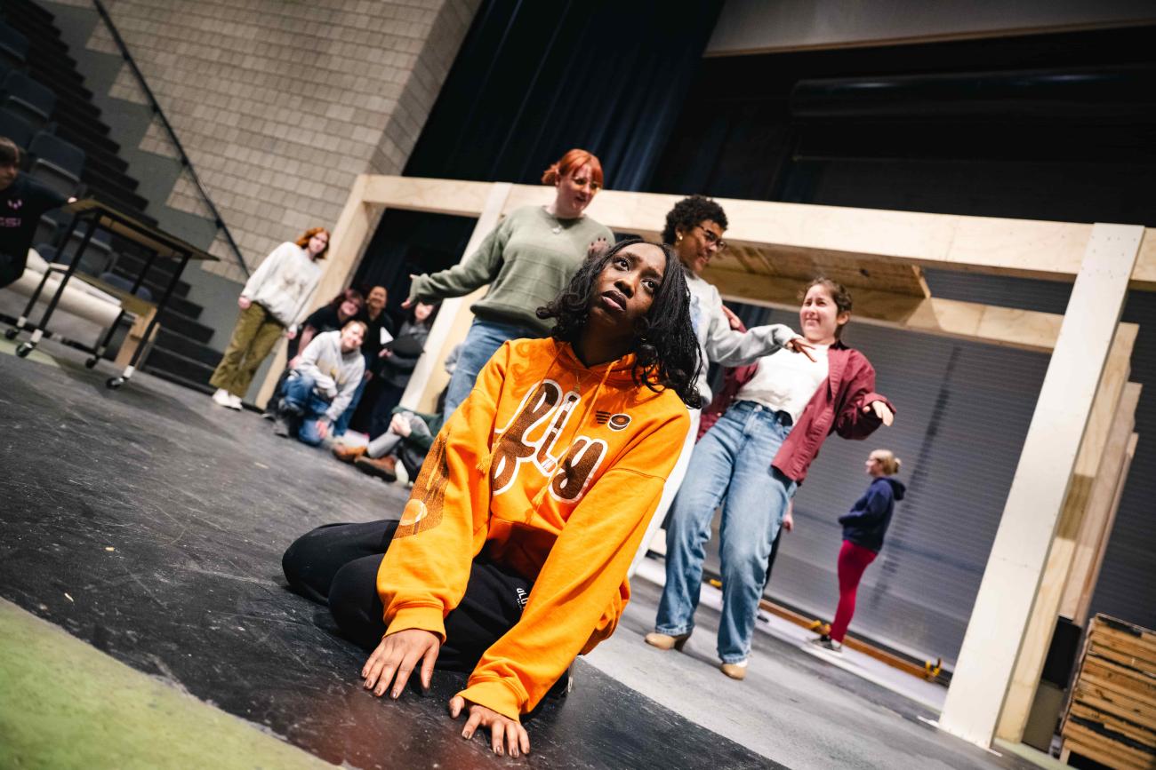 A student kneels on the stage looking off into the distance dramatically during a rehearsal of Into the Woods.